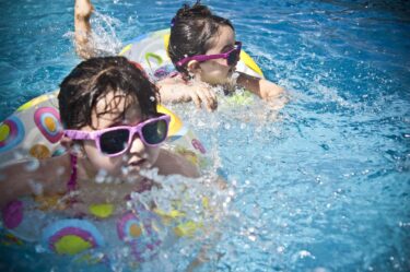 dzieci p艂ywaj膮 w basenie z okularami przeciws艂onecznymi